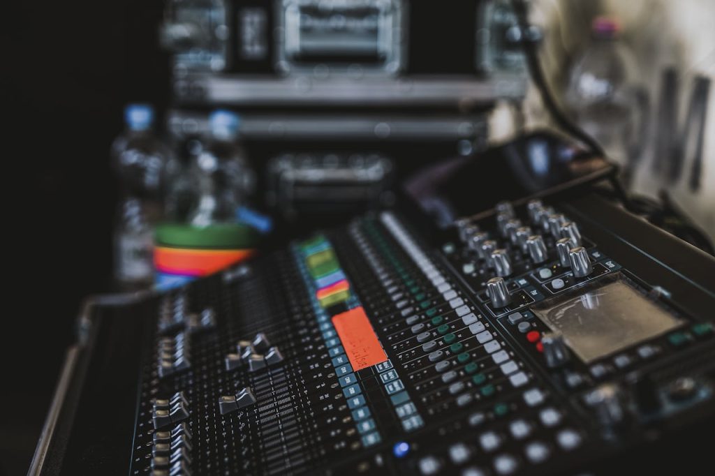 Close-up of a professional audio mixer with various knobs and sliders in a music studio setting.