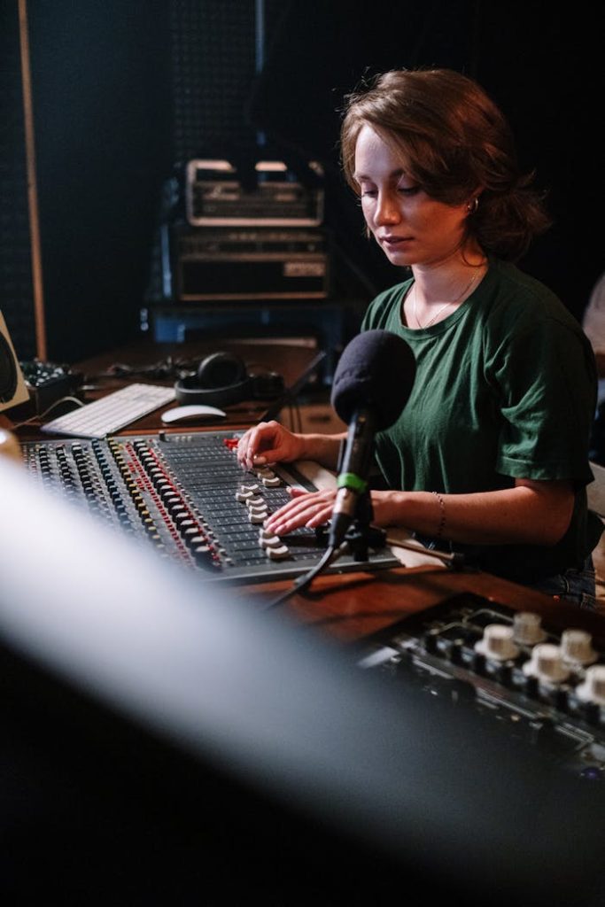 A focused woman manages an audio mixer in a recording studio setting.